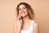Young blonde woman with curly hair isolated on beige background with cotton pad for removing makeup from her face