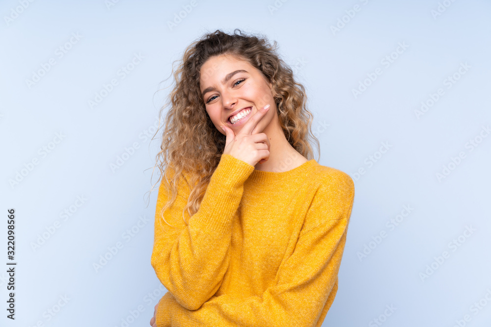 Young blonde woman with curly hair isolated on blue background smiling Young blonde woman with curly hair isolated on blue background smiling