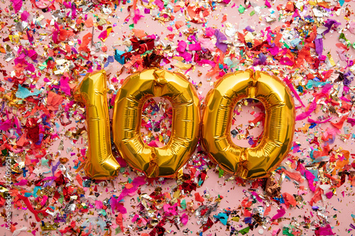 Number 100 gold birthday celebration balloon on a confetti glitter background photo