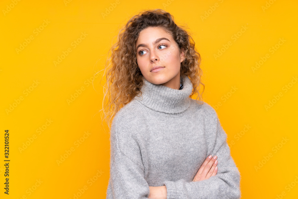Young blonde woman with curly hair wearing a turtleneck sweater isolated on yellow background portrait Young blonde woman with curly hair wearing a turtleneck sweater isolated on yellow background portrait