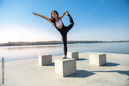 Sportive woman doing yoga exercise in the park, near the lake at daytime. Healthy lifestyle concept.
