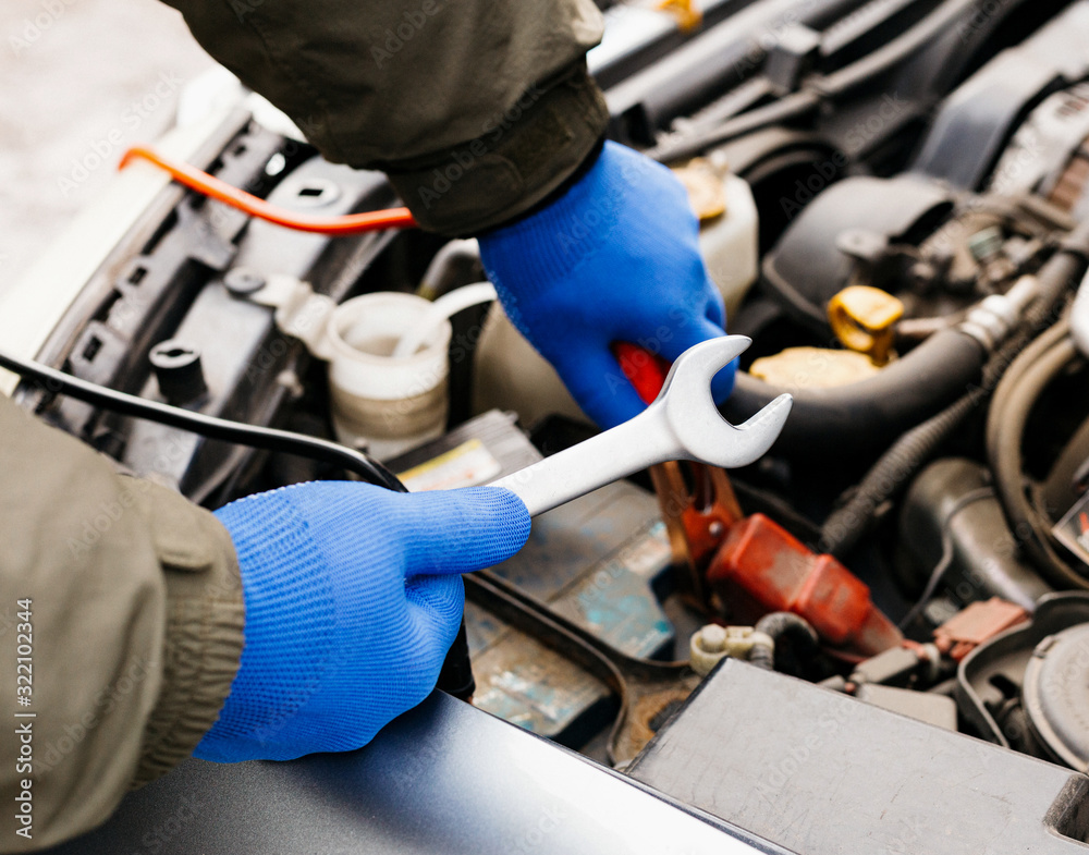 Car mechanic engineer using a wrench in process of fixing a car. Male hands of car mechanic with a wrench working in garage. Man in gloves working in car repair service station. Car mechanic engineer using a wrench in process of fixing a car. Male hands of car mechanic with a wrench working in garage. Man in gloves working in car repair service station.