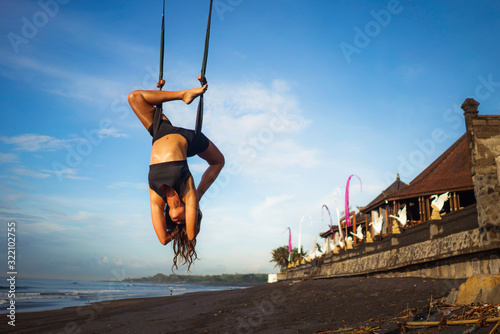 aero yoga beach workout - young attractive and athletic woman practicing aerial yoga exercise training acrobatic  body postures on blue sky over sea in Bali island photo