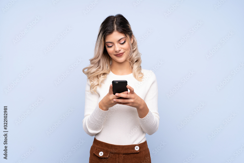 Young teenager girl over isolated blue background sending a message with the mobile