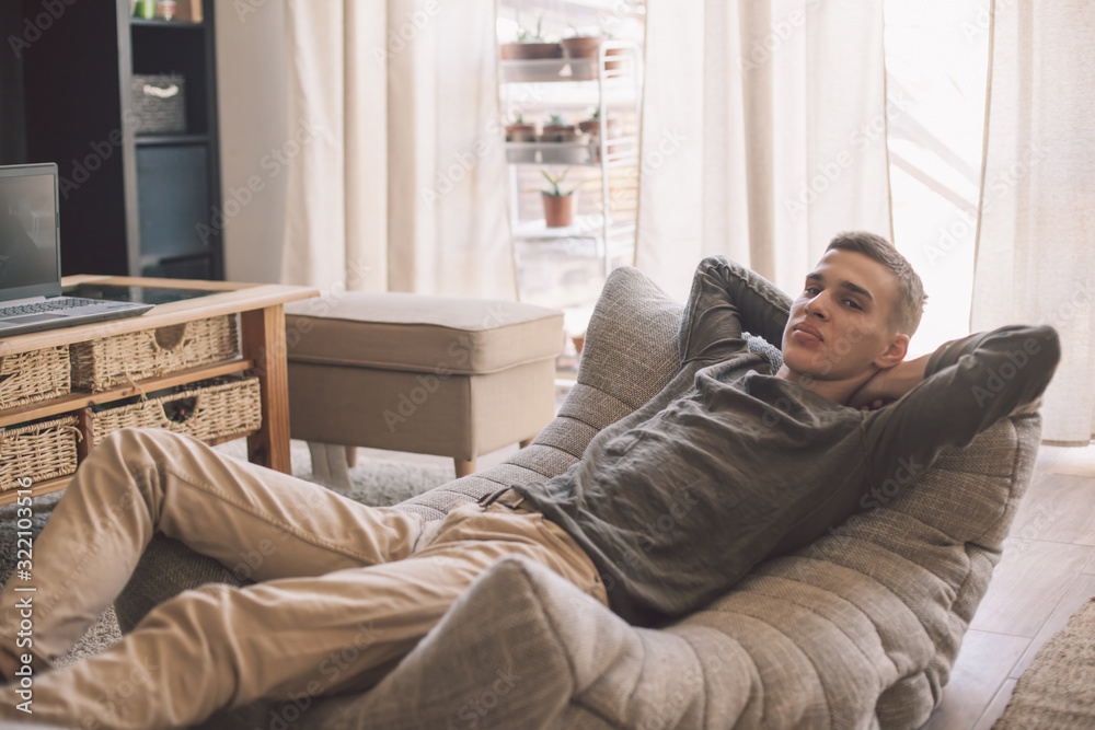 Handsome teenage guy relaxing on modern soft couch at home in living room