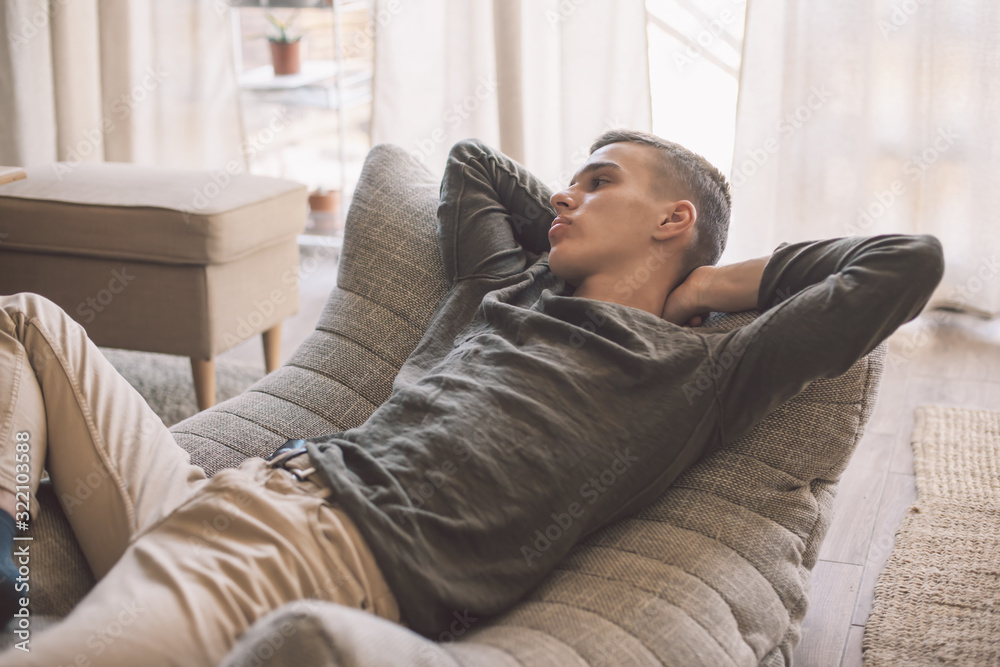 Handsome teenage guy relaxing on modern soft couch at home in living room Handsome teenage guy relaxing on modern soft couch at home in living room