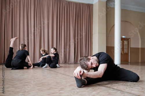 Horizontal shot of professional dance team members doing neccessary warming up exercises in morning photo