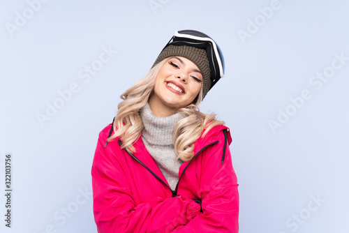 Skier teenager girl with snowboarding glasses over isolated blue background laughing © luismolinero