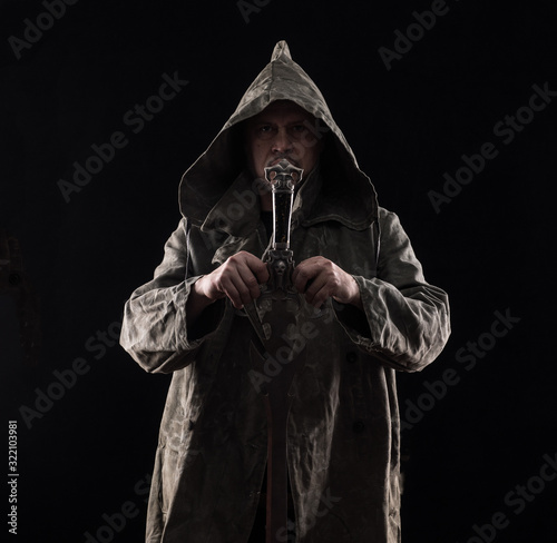 monk in a hood with a sword on a black background photo