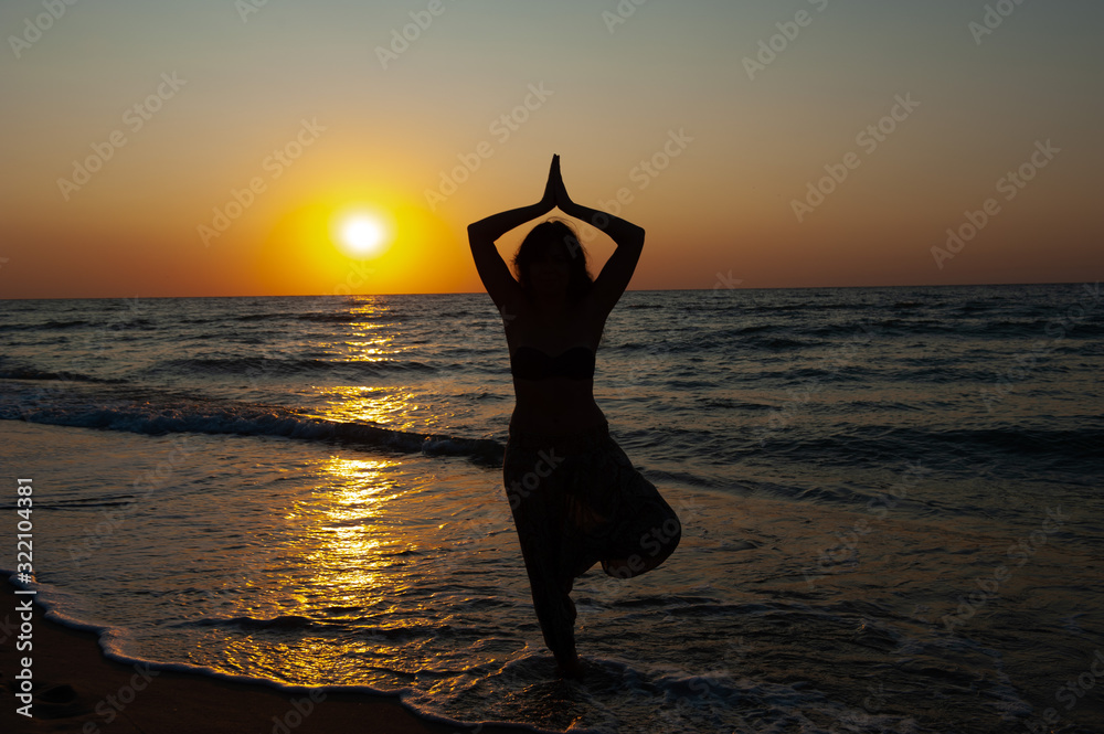 A girl stands in a yoga tree pose at sunset, sunrise