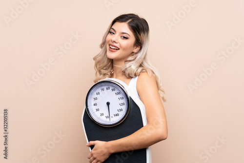 Teenager girl with weighing machine over isolated background holding weighing machine with thumb up