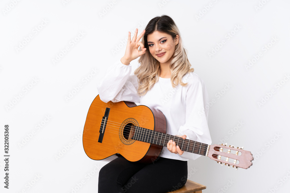 Teenager girl with guitar over isolated white background showing ok sign with fingers Teenager girl with guitar over isolated white background showing ok sign with fingers