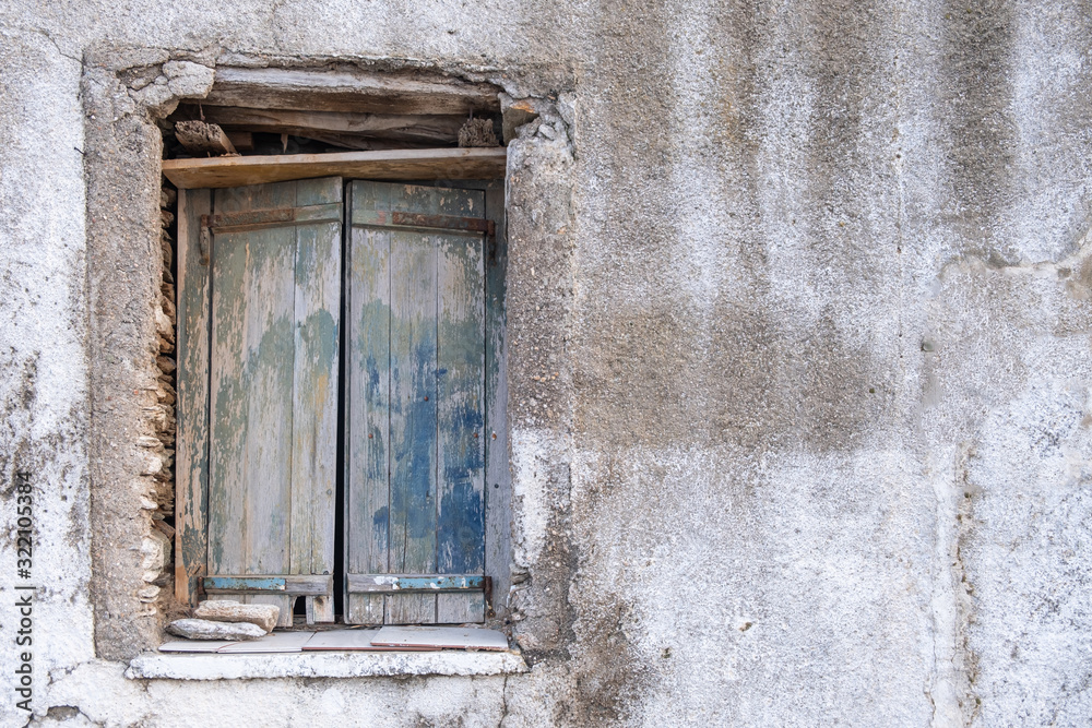 Old double closed wooden shutters. Rusty hinges on peeled planks,  stones keep the window shut. Wall blank and faded. Copy space.