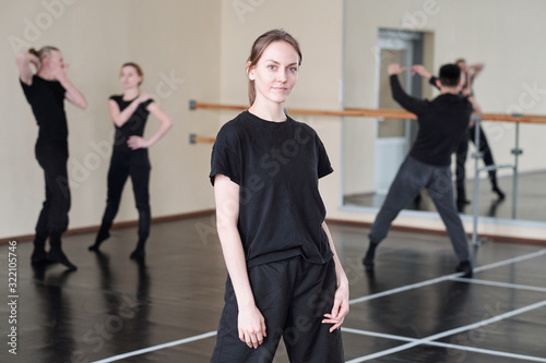Horizontal medium long portrait of young woman wearing stylish black outfit standing in rehearsal studio looking at camera photo