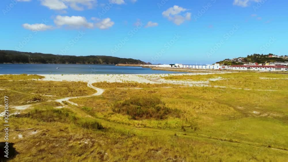 Peaceful landscape with vivid colors of grass field near sandy bank of calm clear water of shallow lagoon in Viveiro Covas, Spain Peaceful landscape with vivid colors of grass field near sandy bank of calm clear water of shallow lagoon in Viveiro Covas, Spain