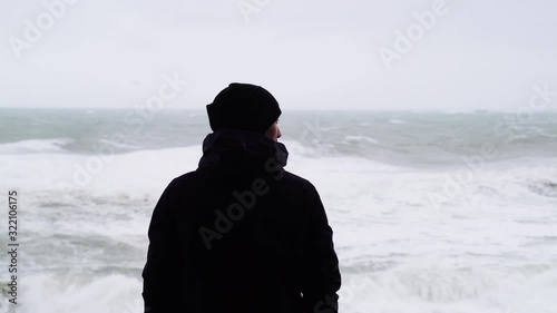 The man looks at the raging sea. A man is watching the storm. Silhouette of a man. Severe stormy sea. Big waves. Windy rainy weather. View of the dramatic ocean. The wind is blowing.