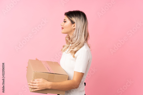 Teenager girl over isolated pink background holding a box to move it to another site