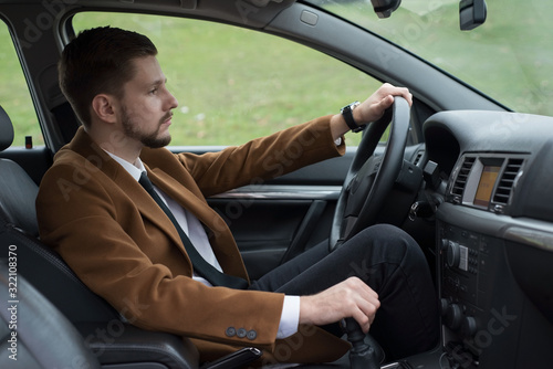 portrait of a young bearded guy in a suit driving a car