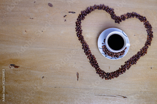 Cup of coffee on wooden table with a heart of coffee beans photo