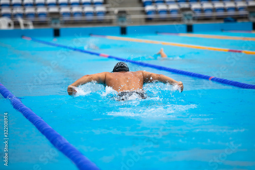 Athletic man swimming in butterfly style in the swimming pool with clear blue water.
