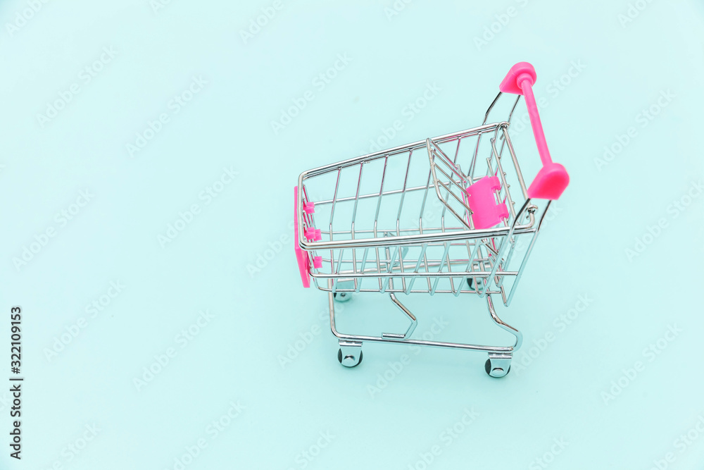 Small supermarket grocery push cart for shopping toy with wheels isolated on blue pastel colorful trendy background Copy space. Sale buy mall market shop consumer concept. Small supermarket grocery push cart for shopping toy with wheels isolated on blue pastel colorful trendy background Copy space. Sale buy mall market shop consumer concept.