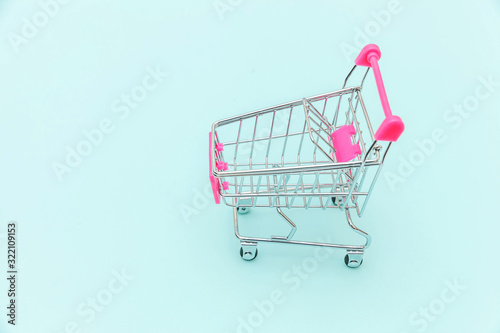 Small supermarket grocery push cart for shopping toy with wheels isolated on blue pastel colorful trendy background Copy space. Sale buy mall market shop consumer concept.