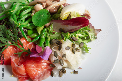 Close-up of dish of marinated salmon in beet and dill. Perona green beans, pickled fennel, green asparagus, marinated mushrooms and pumpkin seeds. Isolated image photo