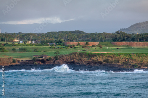 Nawiliwili, Kauai, Hawaii, USA. - January 16, 2020: Early morning light on Timbers Kauai Ocean Golf Course with ocean crashing on black lava rocs under dark gray sky. Belt of green trees on horizon.