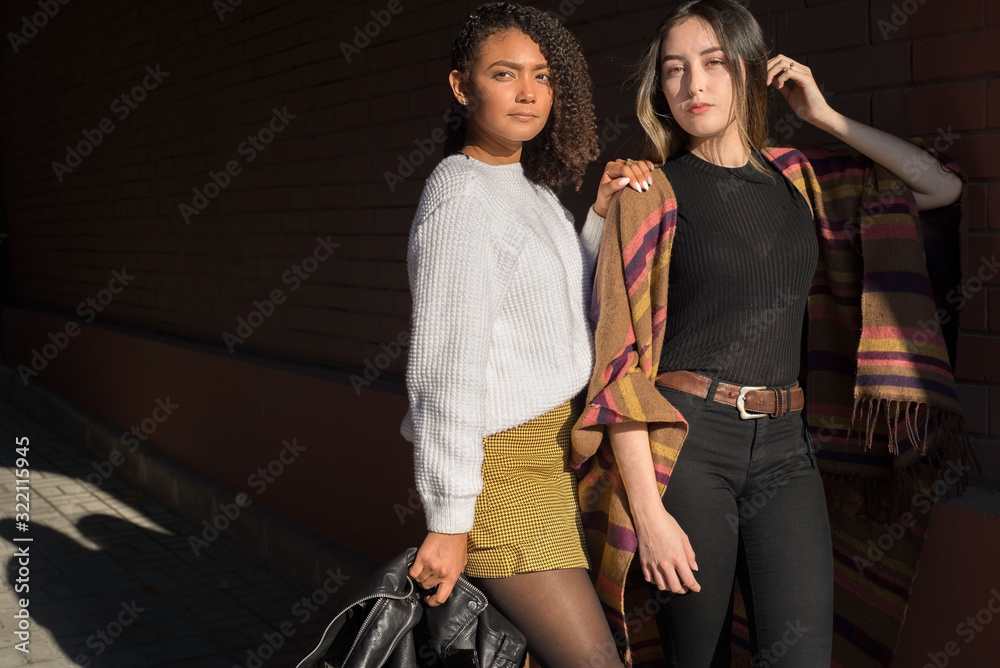 Obraz premium Portrait of two beautiful fashionable Hispanic girls, happy smiling posing for the camera. Autumn street art photo. Y, Z
