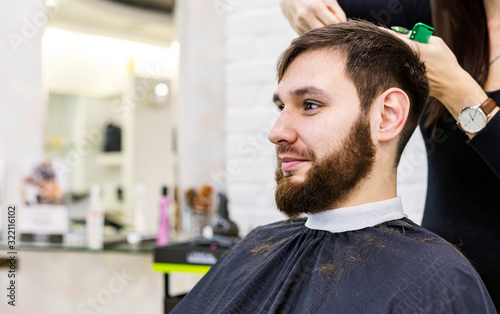 Hairdresser doing haircut for male client, man with beard using professional hairdresser tools, equipment on hairdresser work space, workplace. Hairdresser service.Barbershop hair cut, beard trimming.