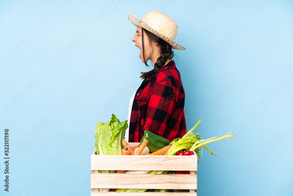 Young farmer Woman holding fresh vegetables in a wooden basket laughing in lateral position