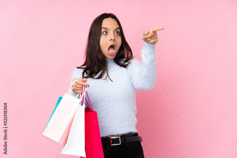 Young woman with shopping bag over isolated pink background pointing away Young woman with shopping bag over isolated pink background pointing away