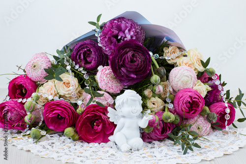 on a light background a bouquet of ranunculuses  roses  transparent beads and a white angel