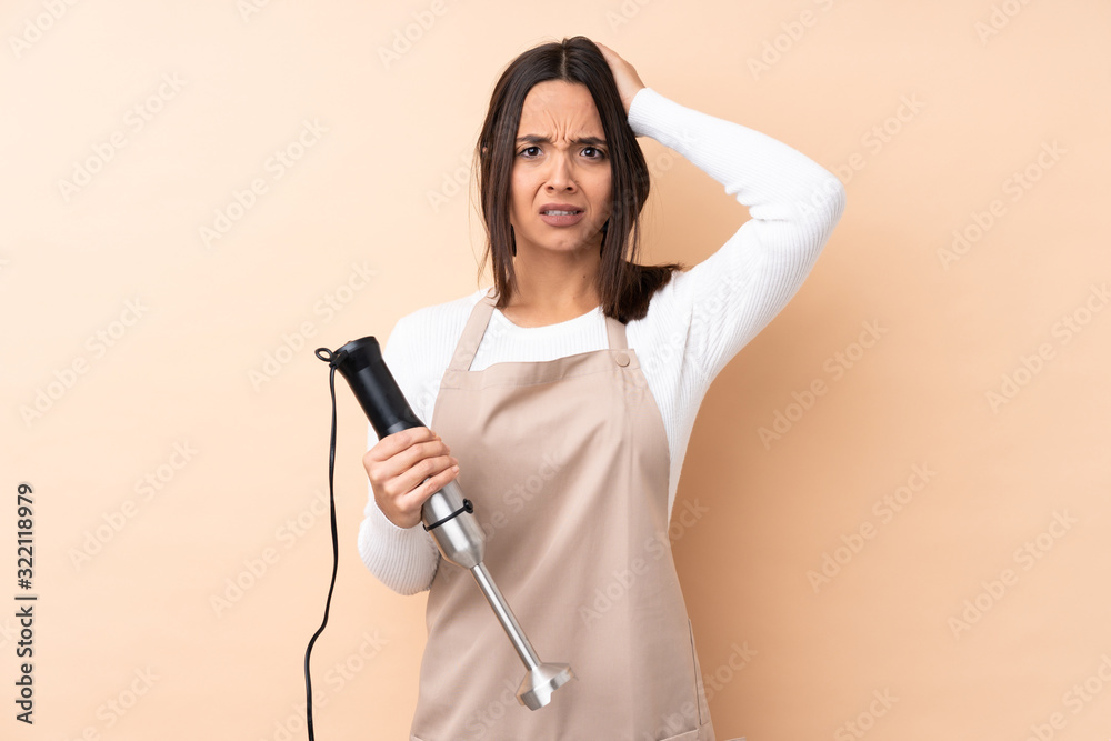 Young brunette girl using hand blender over isolated background frustrated and takes hands on head