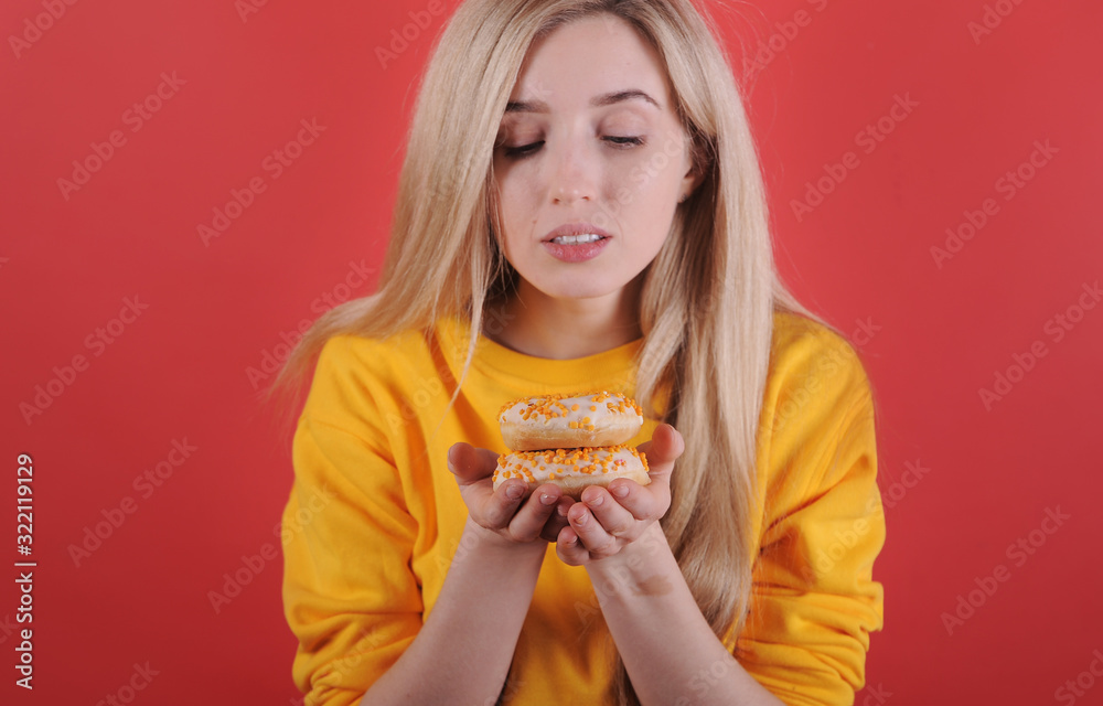 Smiling caucasian woman in yellow sweater with donuts posing on red background. Smiling caucasian woman in yellow sweater with donuts posing on red background.