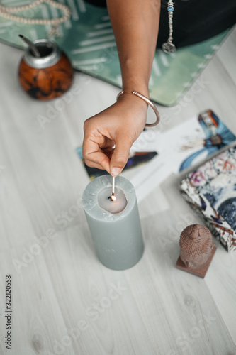 A woman's hand lights a candle for meditation in yoga. The atmosphere of relaxation and Zen. Exercise for achieving clarity of mind and perfect body. Wooden floor, soft morning light