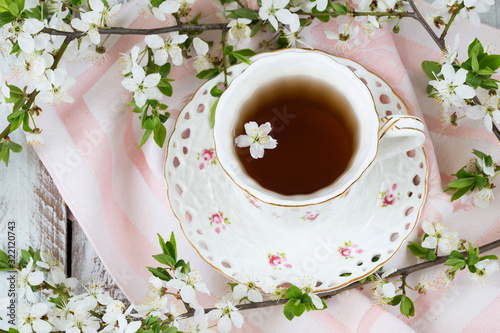 cup of tea, napkin and branches of blossoming cherry closeup on white wooden background