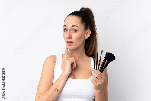 Young brunette woman over isolated white background holding makeup brush