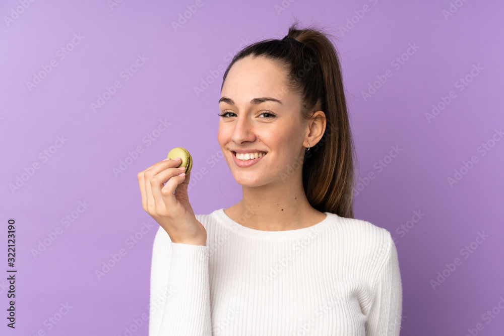 Young brunette woman over isolated purple background holding colorful French macarons Young brunette woman over isolated purple background holding colorful French macarons