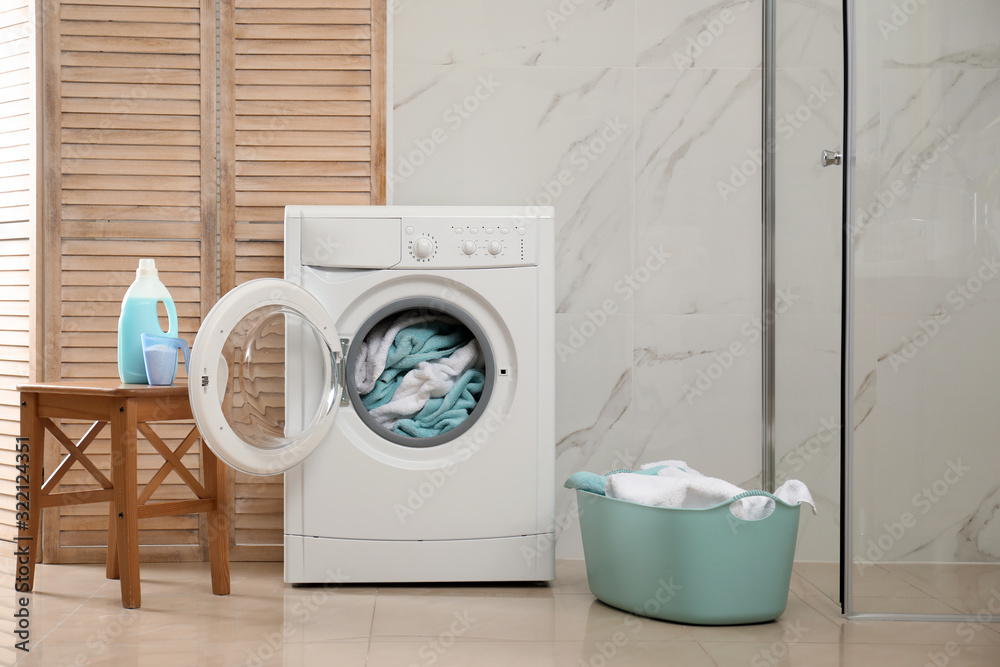 Modern washing machine with towels in bathroom Modern washing machine with towels in bathroom