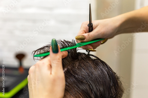 Female hairdresser hands doing haircut for male client using professional hairdresser tools scissors, brush on hairdresser work space. Hairdresser service. Beauty salon hair cut service. Close up