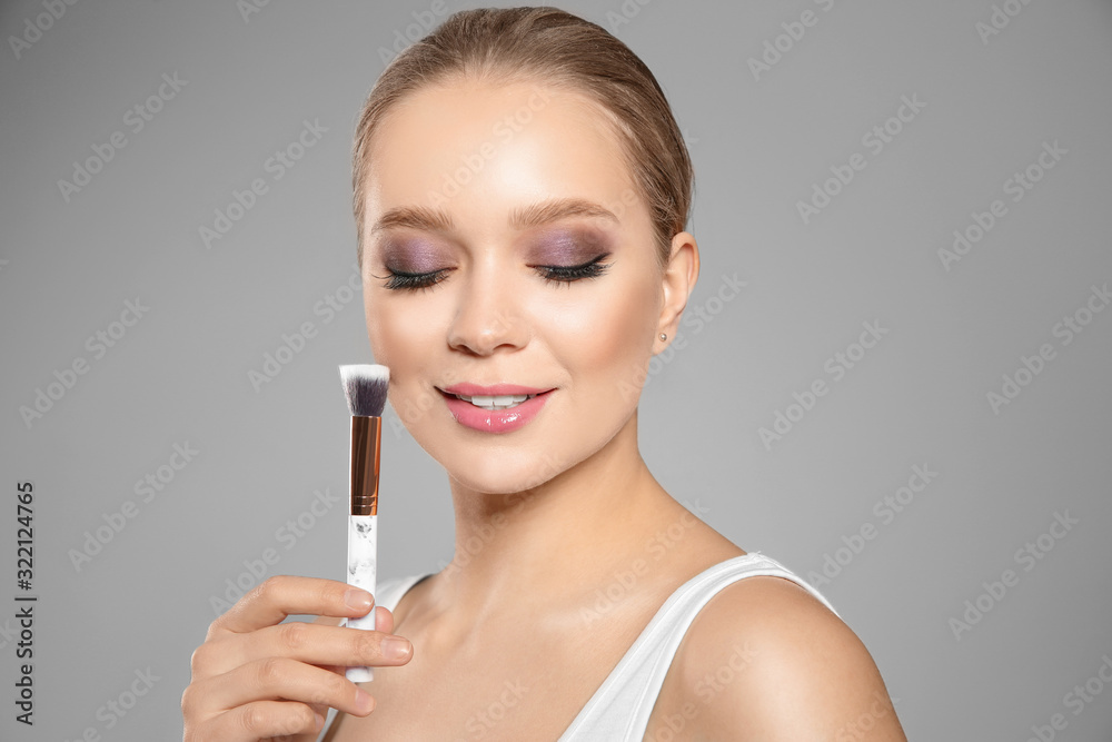 Beautiful woman applying makeup with brush on light grey background Beautiful woman applying makeup with brush on light grey background