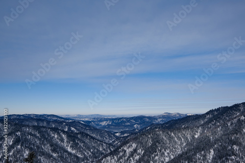 Winter mountain landscape. Snowy mountains overgrown with taiga against the blue sky. Russia. Siberia. Altai Republic.