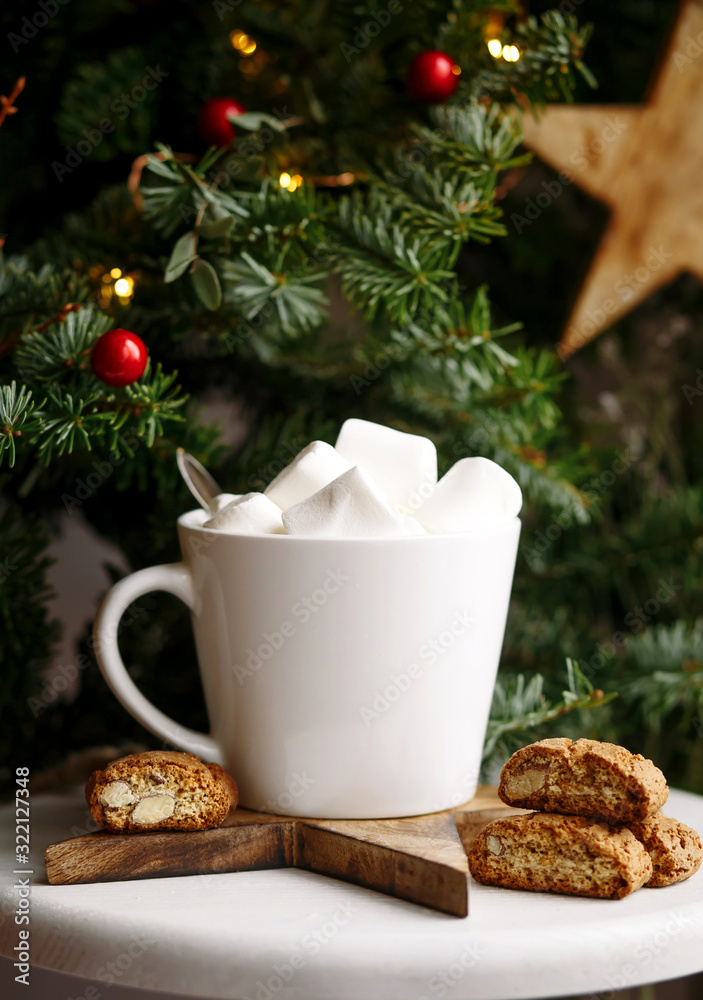 Coffee in a white cup with marshmallows. Morning festive coffee with traditional Italian cantuccini almond cookies. A cup of coffee on a background of green fir branches on a white stand. Coffee in a white cup with marshmallows. Morning festive coffee with traditional Italian cantuccini almond cookies. A cup of coffee on a background of green fir branches on a white stand.