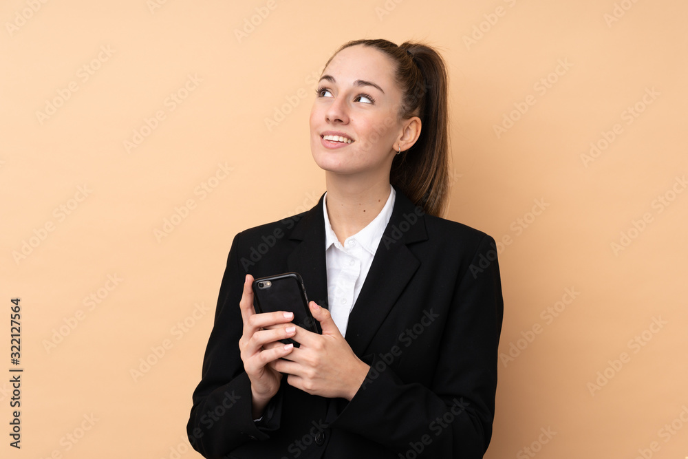 Young business woman using mobile phone over isolated background looking up while smiling Young business woman using mobile phone over isolated background looking up while smiling