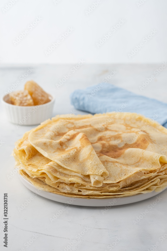 Crepes, thin pancakes with honey on a white plate. Marble background. Close up.