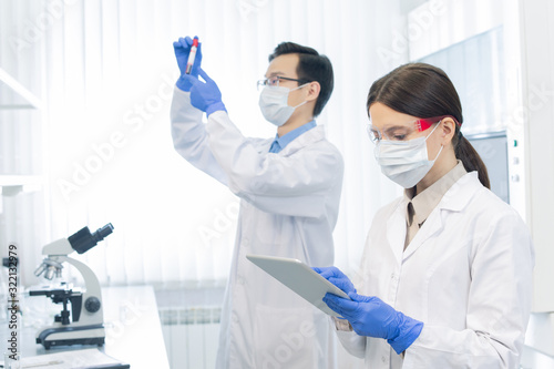 Two young scientists wearing protective masks and gloves working on new medicaments in modern laboratory photo