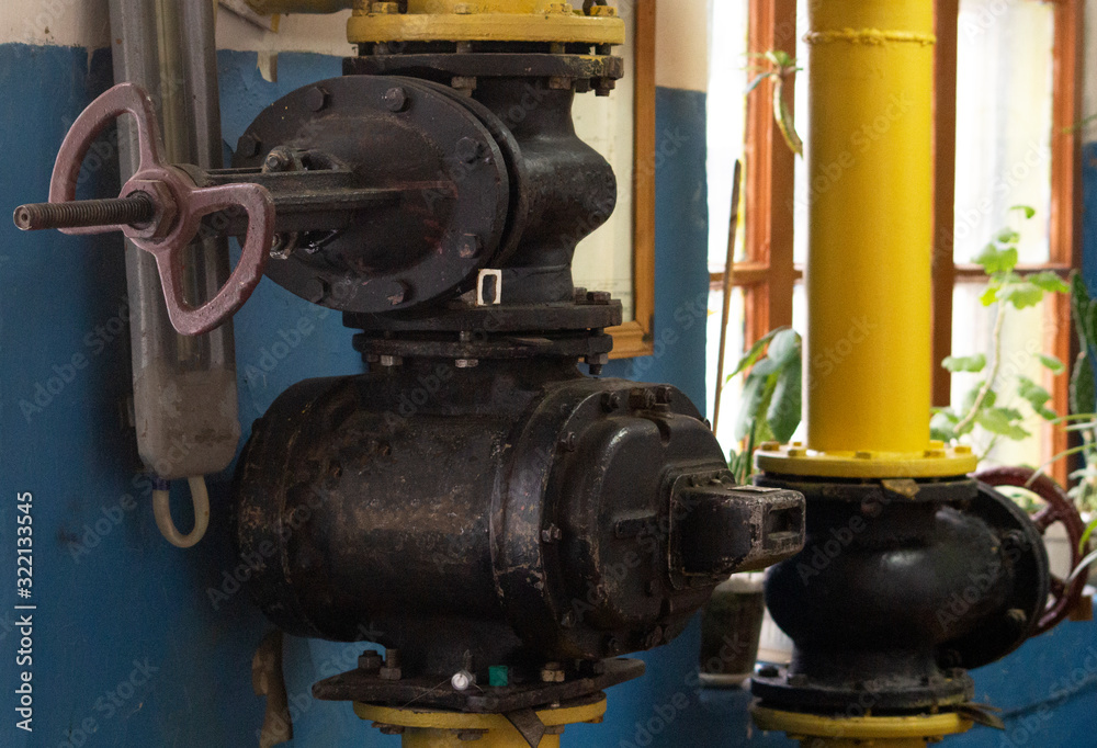 In the foreground is a black gate valve with a diameter of 150 millimeters above the old gas meter in the boiler room. In the background is another valve.