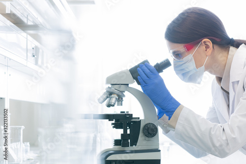 Horizontal side view shot of unrecognizable female medical scientist examining specimen using microscope in modern laboratory