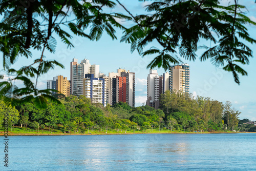 View of a city lake through the tree leaves. Lake surrounded by nature and few buildings on the background. Photo of the Igapo lake, Londrina PR Brazil. © Vinícius Bacarin